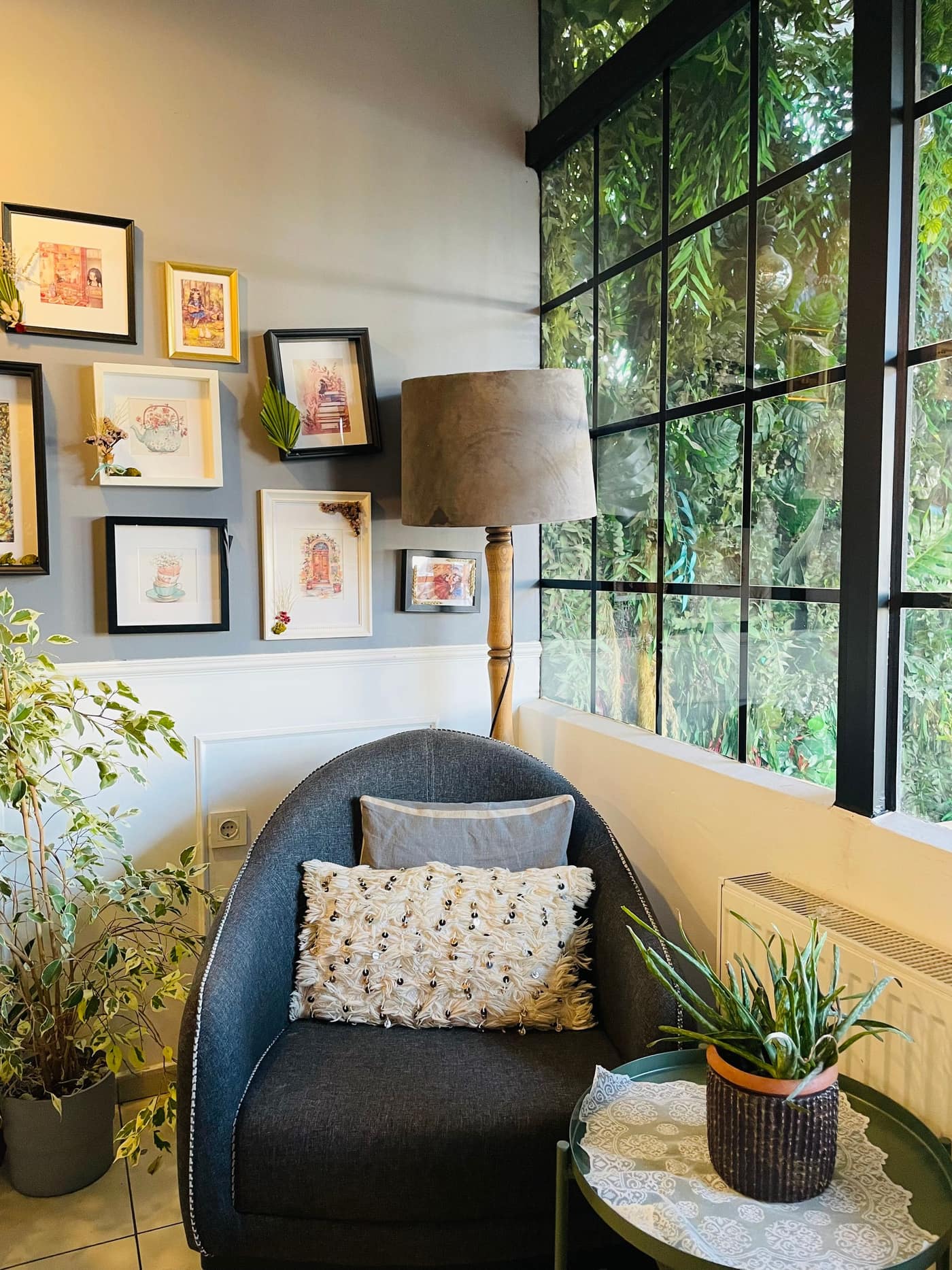 Un fauteuil près d'une grande fenêtre, entre plantes et cadres au mur